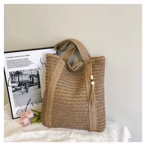 Detail of hand-woven straw tote bag with beaded tassel charm on white fabric