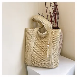 Detail of hollow woven straw tote bag with decorative tassel and wooden bead charm