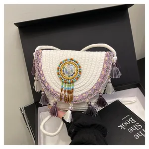 Détail d'un sac besace tissé bohème avec pompons violets et broderie perlée