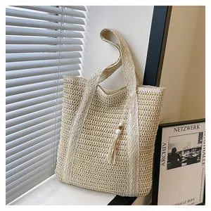 Detail of hollow woven straw tote bag featuring long tassels and white bead accents