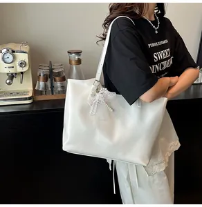 Dettaglio di una borsa tote bianca con fiocco in pizzo e ciondoli di perle al caffè