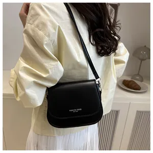 Detailed close-up of a minimalist black leather crossbody bag with white fashion typography