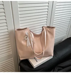 Dettaglio borsa tote rosa chiaro in finta pelle con ciondolo in pizzo e perle su divano