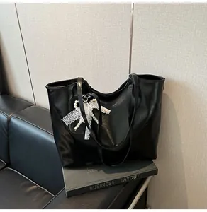 Dettaglio borsa tote nera lucida con fiocco in pizzo bianco e ciondolo con perle fini