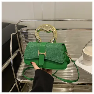 Detail of green bag with sequined flap, golden H buckle, and ring handle in hand