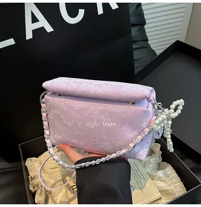 Detail of lavender snake-embossed leather box bag featuring a pearl bow charm and chain strap