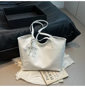 Dettaglio borsa tote bianca con ciondolo fiocco in pizzo e perle su sfondo sobrio