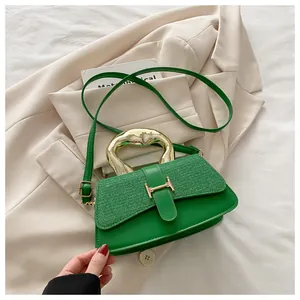 Detail of green handbag with textured leather, gold metal handle and H-shaped lock buckle