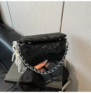 Close-up of black snake texture handbag with pearl pendant and lace charm detail