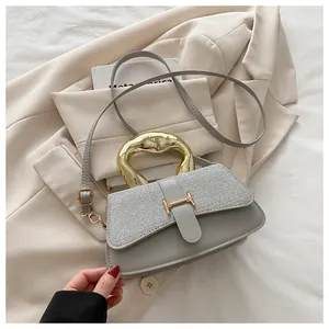 Detail of grey crossbody bag featuring metallic woven flap and unique gold-tone metal handle