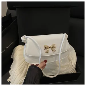 Détail du sac blanc en similicuir avec nœud doré dans un coffret cadeau élégant