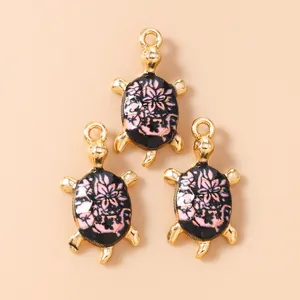 Macro detail of three sea turtle pendants with pink floral enamel and gold plating