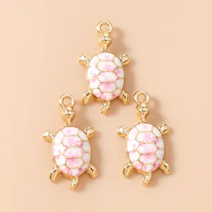Detailed view of sea turtle pendants with pink cherry blossom enamel on gold metal base