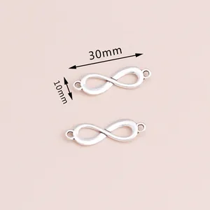 Dijes de infinito plateados de 30mm para creación de joyas DIY en fondo rosa suave