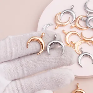 Macro shot of gold and silver crescent moon charms with loops on a pink background