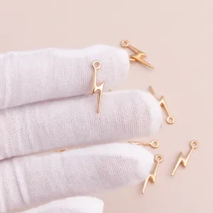 Polished gold lightning bolt charms for DIY jewelry making shown held by a gloved hand