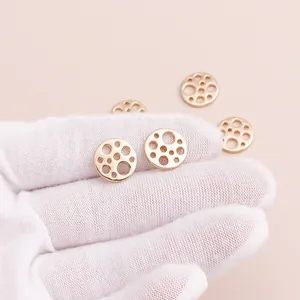 Golden hollow geometric round charms for DIY jewelry making displayed on a hand