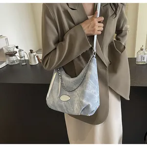 Detail of acid wash denim hobo bag with silver chain strap and metal emblem