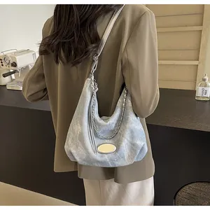 Detail of blue denim hobo bag with silver chain and metal plate on shoulder strap