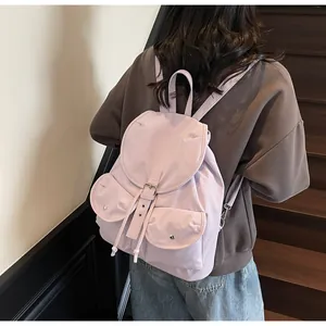 Détail d'un sac à dos en nylon lilas montrant les deux poches et le rabat à boucle