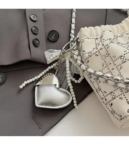 Detalle de colgante para bolso con forma de corazón plateado, perlas blancas y encaje fino