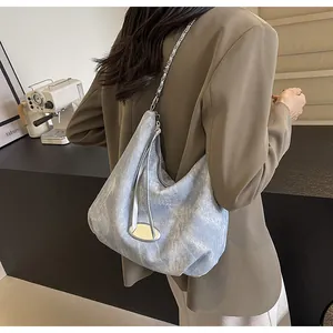 Detailed view of blue denim shoulder bag with metal chain strap on brown blazer