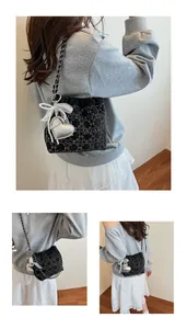 Detalle de bolso acolchado negro con lazo de encaje, dije de corazón y cadena de metal