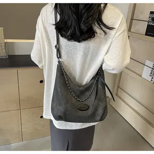 Detail of a charcoal suede hobo bag with a decorative silver chain and leather strap