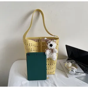 Detail view of yellow bucket bag with laser-cut patterns, plush bear, and tablet for scale