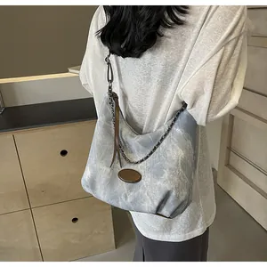 Detail of a large contrast canvas tote bag featuring metal chain straps and leather trim