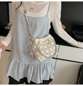 Detalle de bolso tipo cubo acolchado crema con cadena y colgante de lazo con perlas