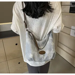 Blue denim crossbody bag with brown leather strap shown on a model in a cozy room