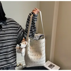 Detail of cream white hollow-out bucket bag with lychee texture and puppy charm