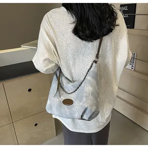 Detail of light blue washed canvas shoulder bag with brown leather strap and chain