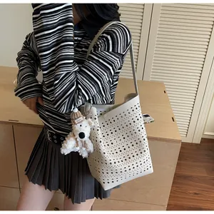 Detailed close-up of white hollow-out bucket bag with a cute plush bear charm accessory