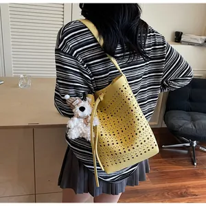 Detail of yellow hollowed-out bucket bag featuring laser-cut patterns and plush dog charm