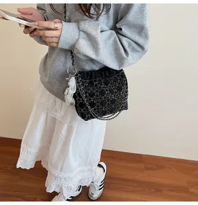 Detalle del bolso tote de terciopelo negro con pedrería, cadena de metal y dije de encaje
