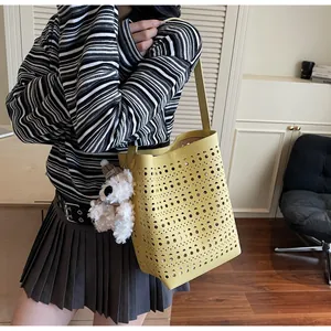 Detail of bright yellow tote bag with hollow patterns and white plush bear charm