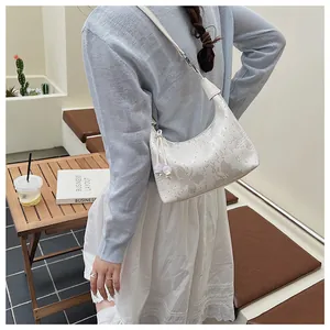 Detail of white PU leather underarm bag featuring butterfly patterns and bead tassels
