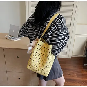 Detail of yellow laser-cut bucket bag with plush charm and long strap in home setting