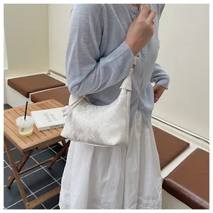 Detail showing creamy white half-moon bag with floral texture and pearl zipper charm