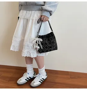 Detalle del bolso de cubo negro con pedrería, patrón de rombos y colgante de lazo y perla