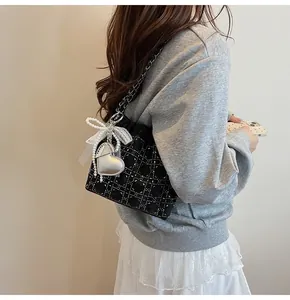Detalle del bolso tote acolchado negro con pedrería y colgante de corazón con perlas
