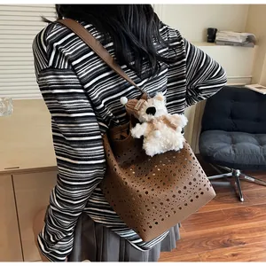 Detail of brown cutout bucket bag with plush bear charm worn over the shoulder