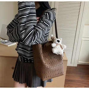 Brown hollow-out bucket bag with cute bear charm shown with striped sweater and pleated skirt