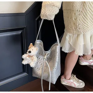 Detail of silver cutout bucket bag with circular holes and a cute bear plush pendant