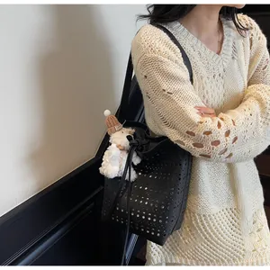 Detail view of black hollow-out bucket bag with laser-cut design and plush bear charm
