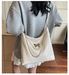 Detail of cream hobo bag with metallic butterfly, pearl chain, and glossy texture