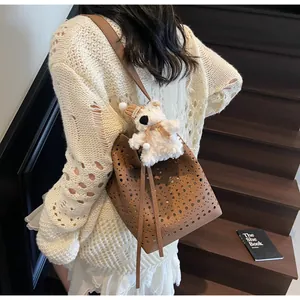 Detail of a brown hollow-out bucket bag with a cute white plush bear charm on the strap