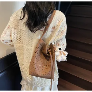 Detail of dark brown cutout leather bucket bag with drawstring and plush bear charm